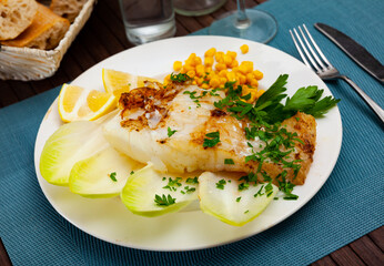 Tasty fried codfish served with endive, greens and corn, Spanish cuisine