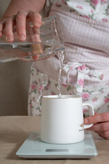 women's hands pour water into a mug standing on kitchen scales at studio