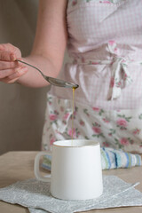 women's hands pour vegetable oil from a teaspoon into a mug at studio