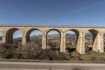 An old stone railway bridge with many arches through which you can see a mountain range next to a...