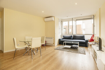 living room with round glass table with white chairs, a sofa under a window and a coffee table with a glass top