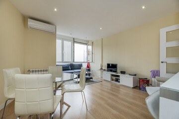 living room with round glass table with white chairs, a sofa under a window, air conditioning on the wall, a coffee table with a glass top