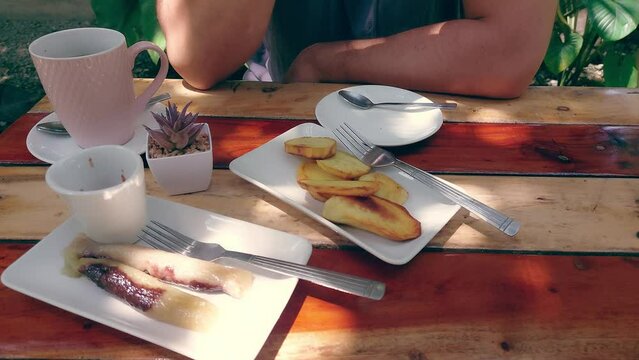 A casual outdoor setting with fried kamote, suman and coffee served on a wooden table and partial view of a person drinking coffee, traditional Filipino snacks for merienda