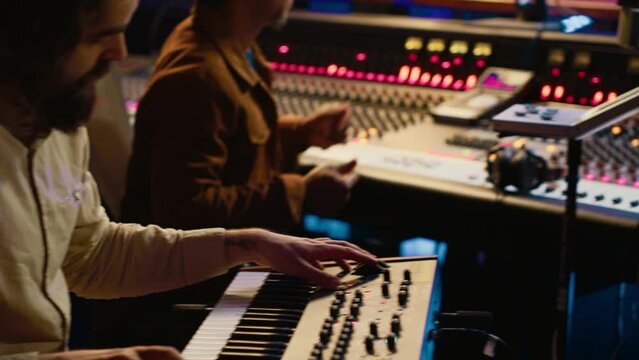 Musician artist playing midi controller synthesizer in recording music studio, composing tracks on mixing console. Singer performing on piano electronic keyboard in control room. Camera A.
