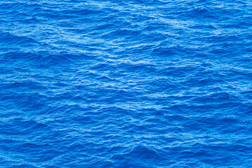 Blue surface of the ocean with gentle ripples on the surface and light reflections.