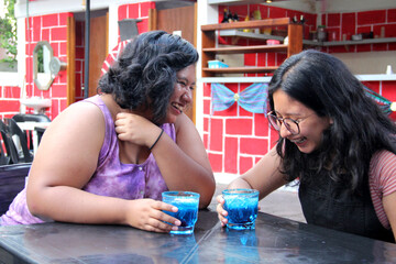 Two young brunette Latin women of 20 years old drink frosty blue cocktail with chili, celebrate by drinking alcohol