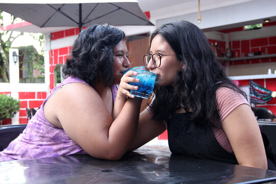 Two young brunette Latin women of 20 years old drink frosty blue cocktail with chili, celebrate by drinking alcohol - Powered by Adobe