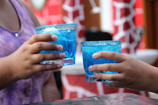 Two young brunette Latin women of 20 years old drink frosty blue cocktail with chili, celebrate by drinking alcohol