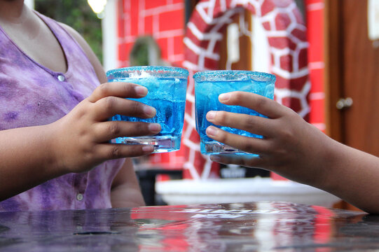 Two young brunette Latin women of 20 years old drink frosty blue cocktail with chili, celebrate by drinking alcohol