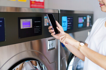 Asian woman using a smartphone payment application to settle for a service cost of using washing...