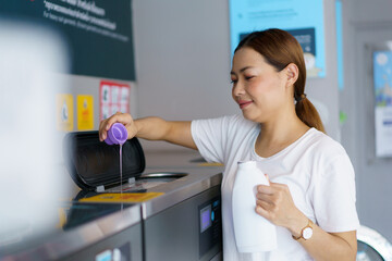 Asian woman pouring liquid detergent into washing machine. 