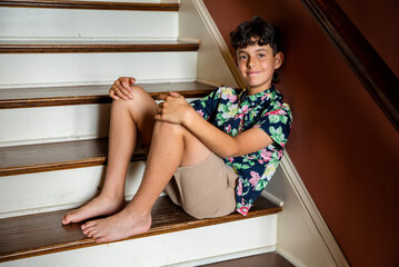 Portrait of a barefoot preteen boy wearing a floral print Hawaiian shirt and khaki shorts, smiling...