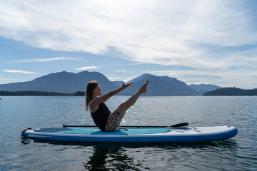 Young woman doing yoga on sup board in the lake.