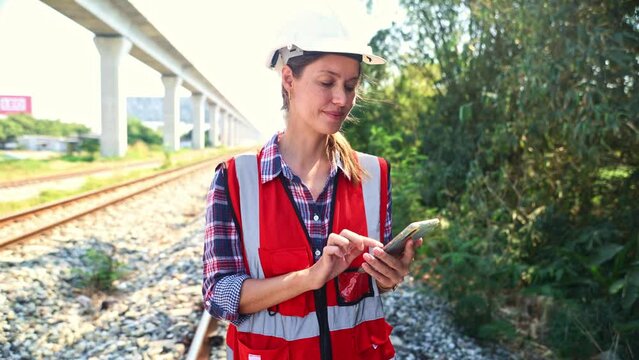 Female caucasian diesel train engineer working in the field outdoors uses smartphone to communicate between herself and her team during maintenance work.