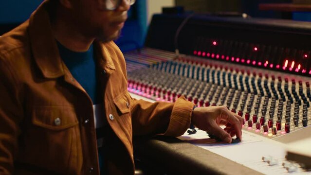 Professional artist singing a song on electro acoustic guitar in studio, recording his music on daw software mixing console in control room. Skilled musician producer composing tracks. Camera A.