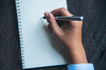 Woman hands writing empty notebook planing meeting agenda on wooden table. Close up women hands...