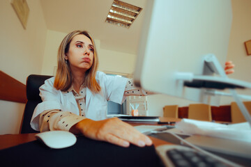 Tired Stressed Doctor Working on a Computer Overtime in Office. Health care worker doing some...