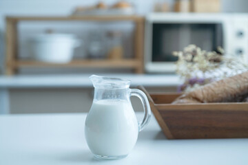 Pitcher of milk prepared for breakfast is placed near a basket of baked bread in the home kitchen,...