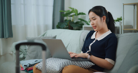 Side view of Asian teenager woman sitting on sofa using laptop for prepare booking hotel and airplane ticket for travel. backpacker travel concept. - 772699735