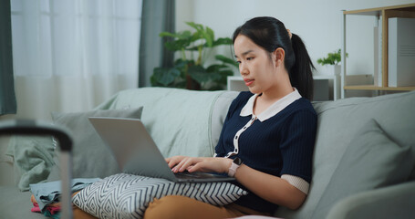 Side view of Asian teenager woman sitting on sofa using laptop for prepare booking hotel and airplane ticket for travel. backpacker travel concept. - 772699757