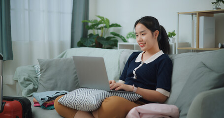 Side view of Asian teenager woman sitting on sofa using laptop for prepare booking hotel and airplane ticket for travel. backpacker travel concept. - 772699772