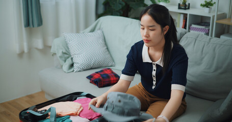 Portrait of Asian teenager woman sitting on sofa packing travel luggage with personal items for traveling trip, Preparation travel suitcase at home. - 772700109