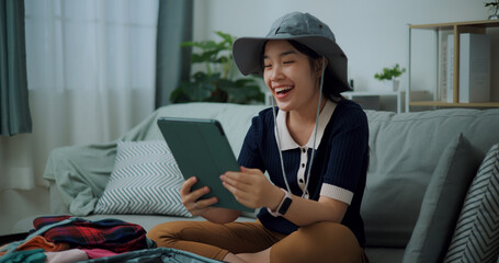 Portrait of Asian teenager woman sitting on sofa video call with friend while packing suitcase luggage for travelling, backpacker travel concept. - 772700397