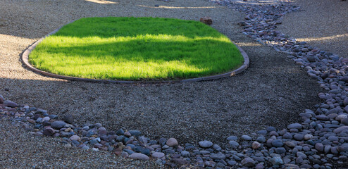 Attractive decorative patch of green grass surrounded by a desert style xeriscaped ground with...