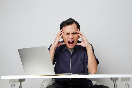 Angry mad asian man in workplace while sitting in front of laptop computer. isolated background