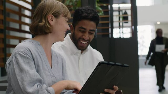 Four young multiracial adults in businesswear smiling while using digital tablet in office