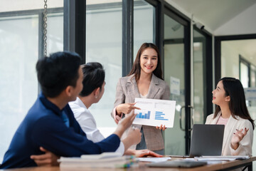 Fototapeta premium Businesswoman presenting graph chart to colleagues in a meeting. Professional corporate team discussion in modern office. Corporate business and teamwork concept.
