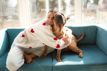 A beautiful young girl is wearing s white sweater with red hearts and jeans, sitting on the coach...