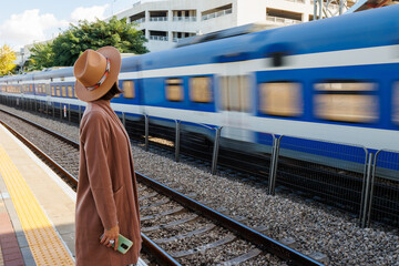 Girl at the railway station. A young woman in a coat and hat stands on the station platform and looks at the train. - 772734329