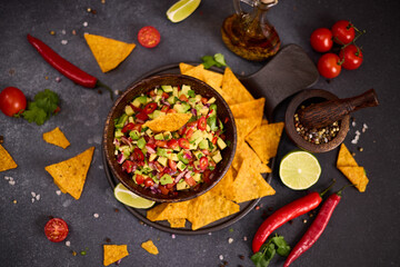 traditional salsa dip snack in wooden bowl and corn nacho chips on a table with ingredients