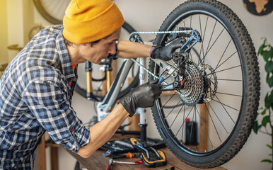 A male bicycle mechanic repairs a mountain bike in a workshop. The concept of preparation for the new season, repair and maintenance
