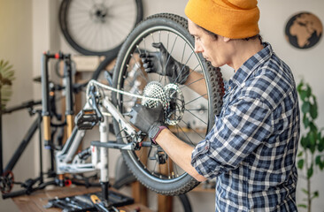 A male bicycle mechanic in the workshop disassembles a mountain bike and repairs it. Maintenance concept, preparation for the new season - 772738946