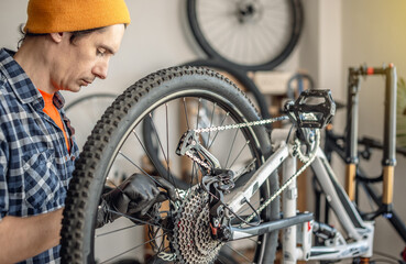 A male bicycle mechanic in the workshop disassembles a mountain bike and repairs it. Maintenance concept, preparation for the new season - 772739328