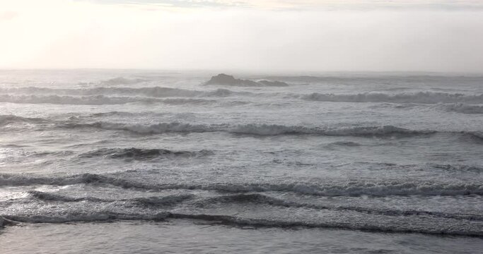 The ocean is rough and choppy, with waves crashing against the shore. The sky is overcast, and the water appears to be a deep shade of blue. Scene is one of turbulence and power