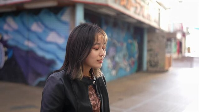 Slow-motion video of an Okinawan woman in her 20s in winter clothes walking on Kokusai Street in Naha City, Okinawa Prefecture with a smile 沖縄県那覇市の国際通りを笑顔で歩く冬服の20代の沖縄県民女性のスローモーション映像