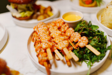 A plate of shrimp skewers with lettuce and sauce, a delicious seafood dish presented on a table with elegant tableware
