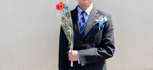 花束を持ったスーツ服装の少年。小学生の卒業式。卒業式の記念ギフト、コサージュ。イベント。子どもの成長。