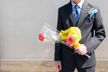 バルーン入り花束を持ったスーツ服装の少年。小学生の卒業式。卒業式の記念ギフト、コサージュ。イベント。子どもの成長。