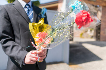 バルーン入り花束を持ったスーツ服装の少年。小学生の卒業式。卒業式の記念ギフト、コサージュ。イベント。子どもの成長。