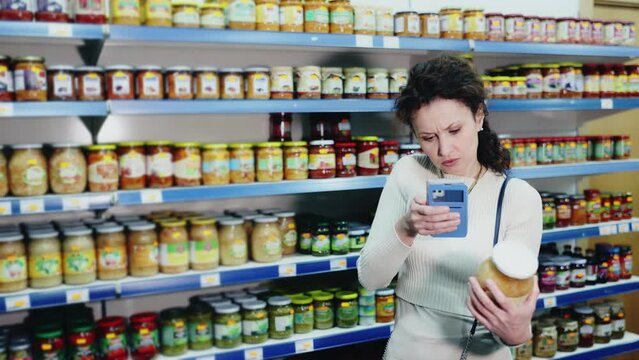 In Russian goods store, woman choose jar of pickled fermented cabbage and photographs label. High quality 4k footage
