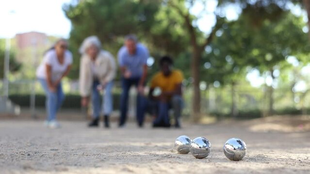  A group of multiracial mature adult people playing patanque game outdoors in a park. High quality 4k footage