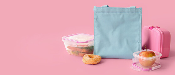 Bag and lunchboxes with delicious food on pink background
