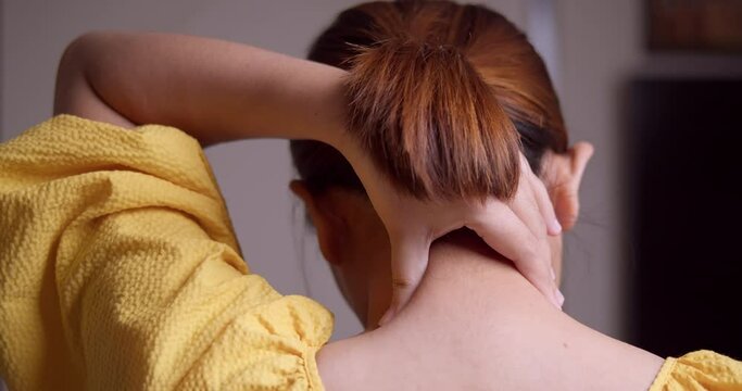 A young woman is pinching her nape as she massages it to relieve herself of the pain that she is feeling around her neck.