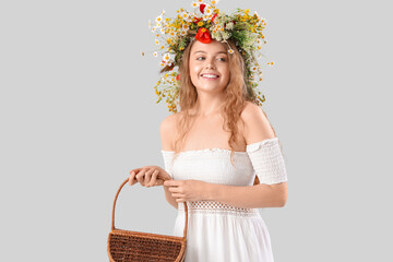 Beautiful young woman in flower wreath and with basket on light background. Summer solstice