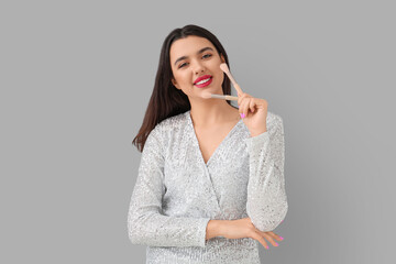 Beautiful young happy woman with makeup brushes on grey background