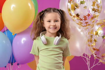 Fototapeta na wymiar Cute little girl with headphones and balloons on purple background